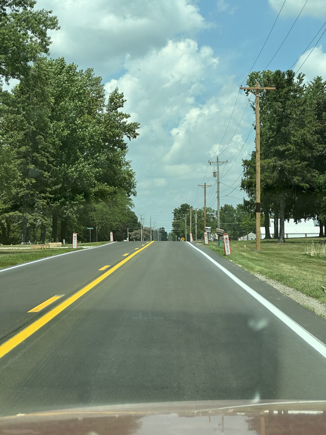 A straight two-lane road running into the distance under a big sky of scattered clouds in rural Indiana.