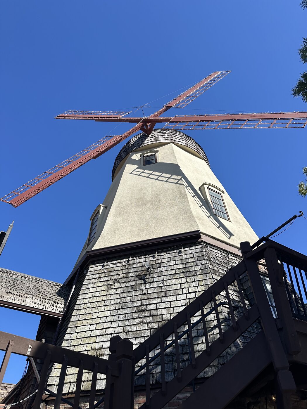 A tall windmill rising over Danish-style architecture under a clear blue sky in Solvang, California.