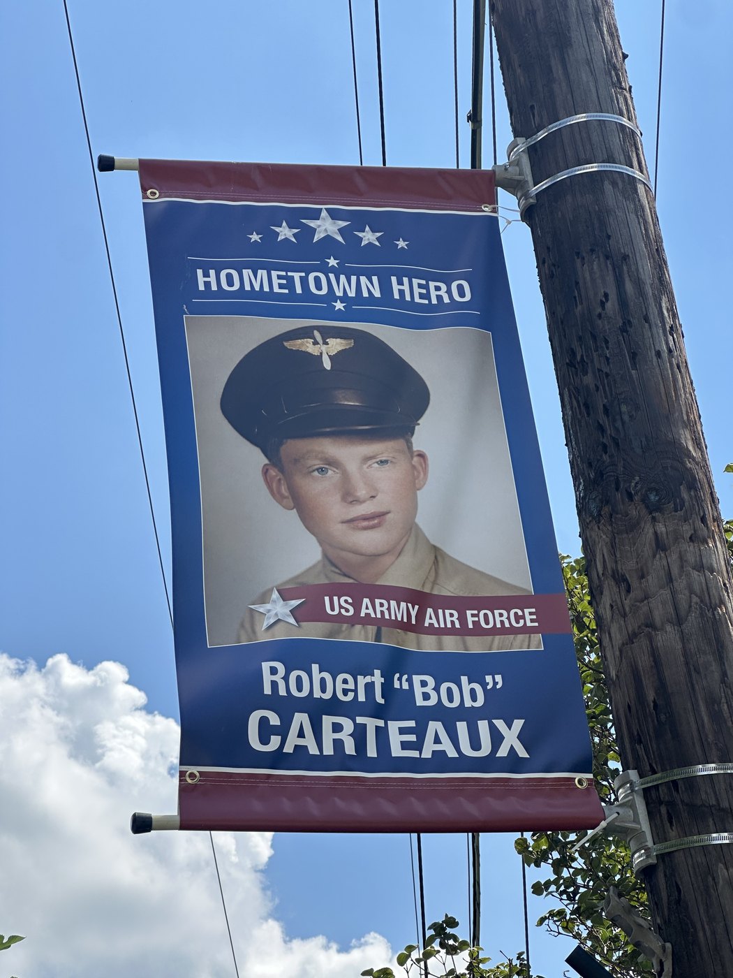 A Hometown Hero banner on a utility pole: a colorized photo of a young Robert “Bob” Carteaux in a US Army Air Force service cap.