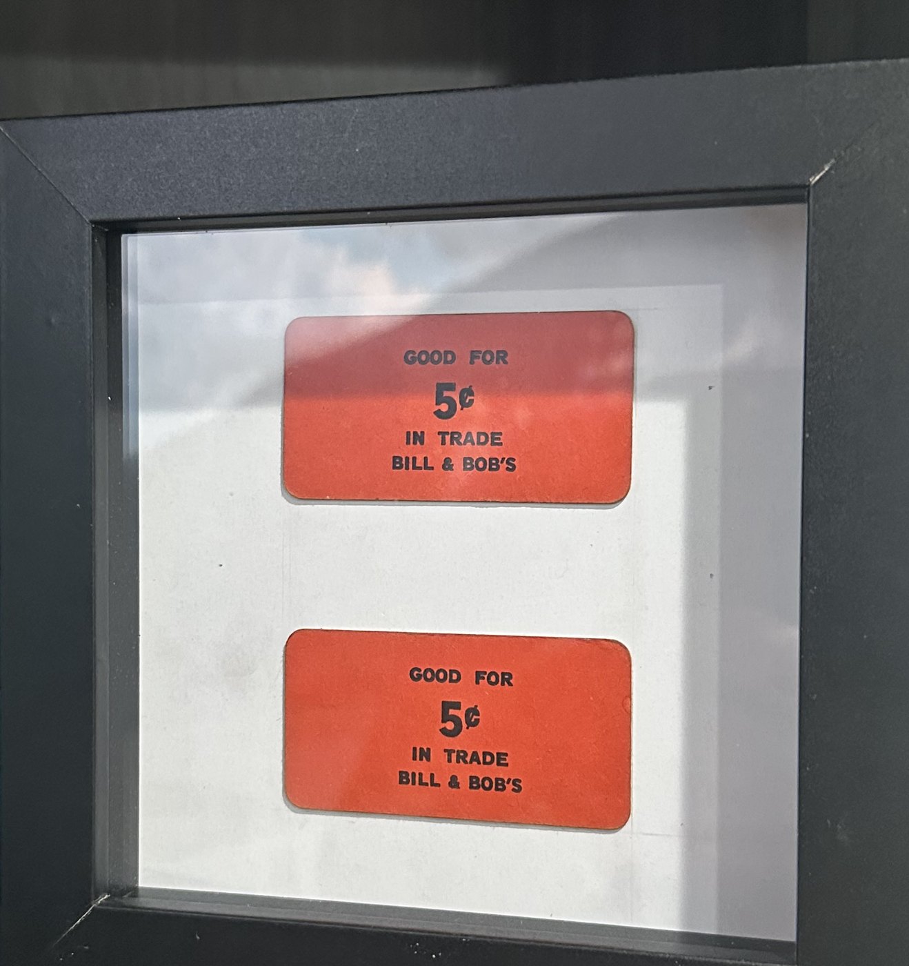 Two red “Good for 5¢ in trade — Bill & Bob’s” tokens mounted in a black shadow box.